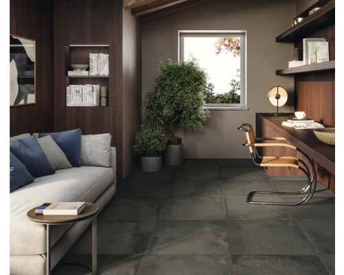 Woonkamer met bank, bureau en donkere vloertegels.