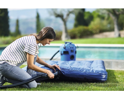 Vrouw pompt luchtbed op met een elektrische luchtpomp in de tuin.