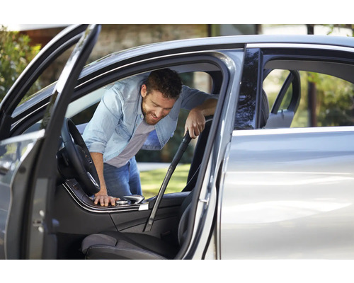 Een man maakt het interieur van een auto schoon met een stofzuiger.