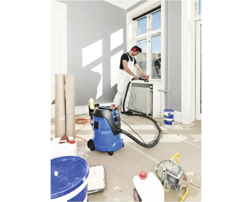 Scene van een kamer met een vakman die een vensterbank schuurt, een stofzuiger en verfcontainers