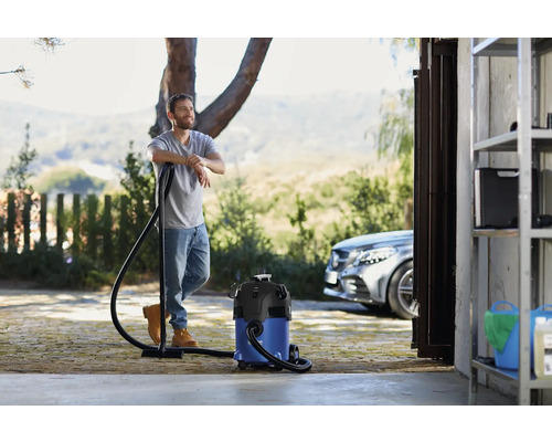 Een man leunt tegen een alleszuiger voor een garage en een auto.