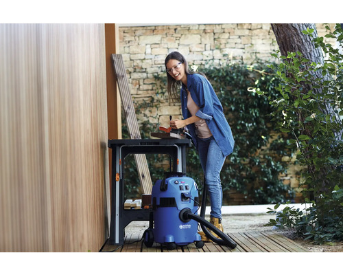 Een vrouw werkt aan een werkbank met een alleszuiger in de buurt.