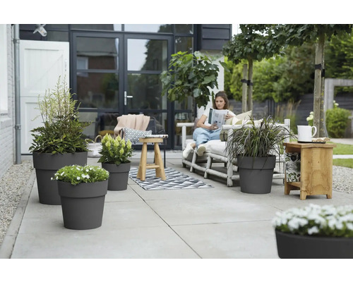 Terras met grijze plantenbakken en een vrouw die een boek leest op een bank