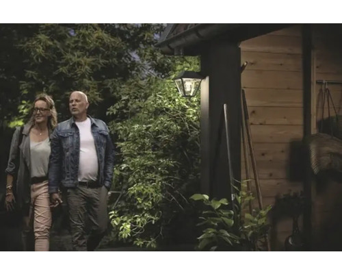 Scène met een verlichte buitenwandlamp aan een gebouw, met twee personen ervoor