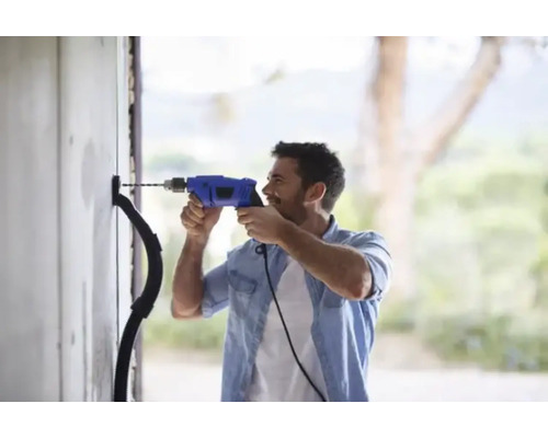 Een man boort met een boormachine een gat in een muur voor een elektriciteitskabel.