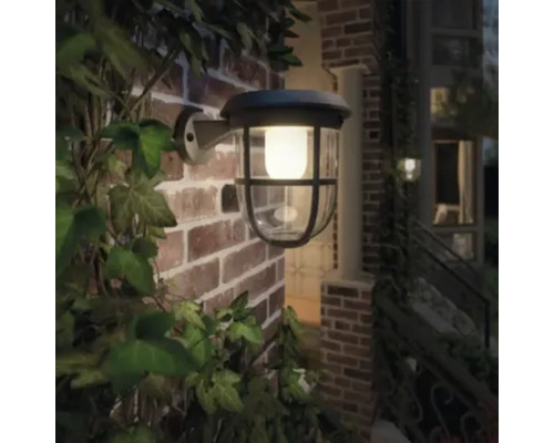 Verlichte buitenmuurlamp op bakstenen gebouw met planten