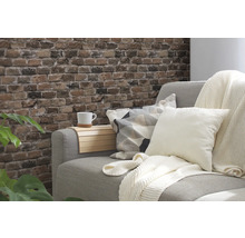 Decoratieve woonkamer met grijze bank, kussens, plaid en muur met baksteenmotief.
