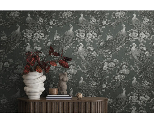 Detailopname van een muur met behang met pauwen en bloemenmotief, met een tafel en decoraties ervoor