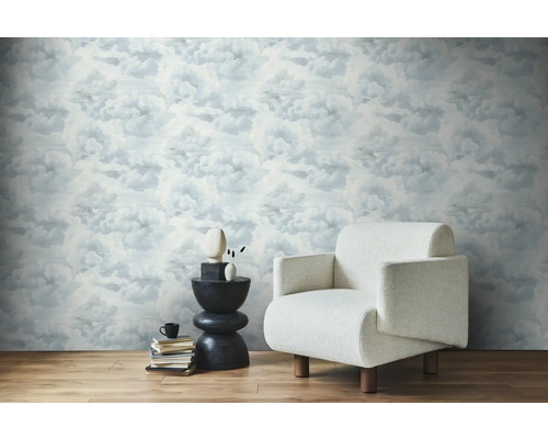 Lichte kamer met wolkenbehang, fauteuil en bijzettafel.