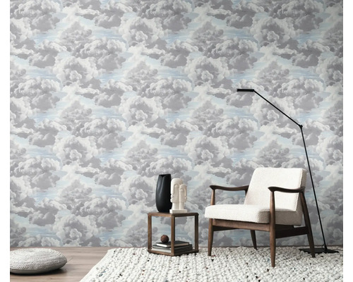 Een kamer met behang met wolkenpatroon, een fauteuil, een vloerlamp en een bijzettafel.