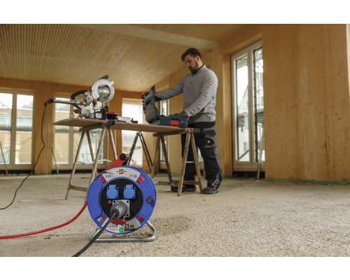 De afbeelding toont een bouwplaats met een kabelhaspel, een verstekzaag en een vakman.