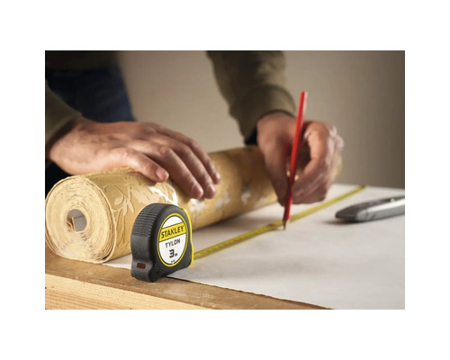 Een persoon meet een rol behang met een meetlint en markeert deze met een potlood.