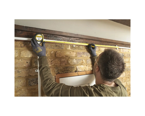 Iemand meet met een meetlint de lengte van een muur.