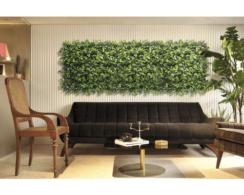 Decoratief interieur met plantenwandpaneel boven een zwarte bank.