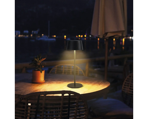 Buitenfoto van een tafellamp op een houten tafel buiten ''s nachts.