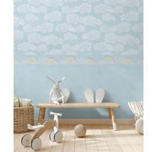 Kinderkamer met wolken- en regenboogpatroonbehang, bank, speelgoed en decoraties voor een heldere en vriendelijke sfeer.