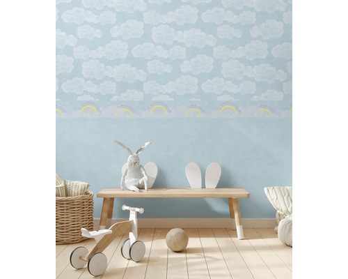 Kinderkamer met wolken- en regenboogpatroonbehang, bank, speelgoed en decoraties voor een heldere en vriendelijke sfeer.