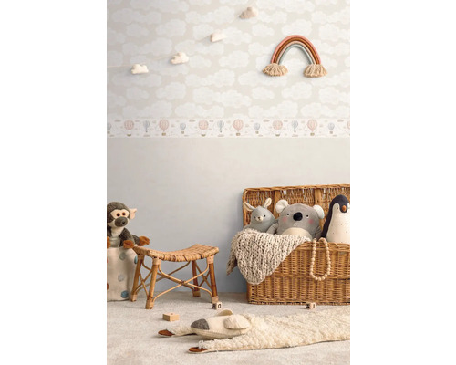 Gedecoreerde kinderkamer met wolkenbehang, regenboog wanddecoratie, rotan krukje en speelgoed in een mand.
