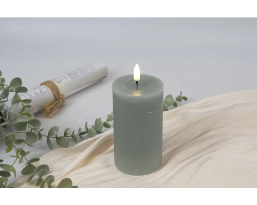 Decoratieve LED stompkaars met planten en een schriftrol op een beige doek