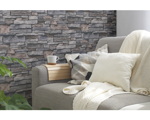 Woonkamer met grijze bank, kussens, deken en steenwandbehang