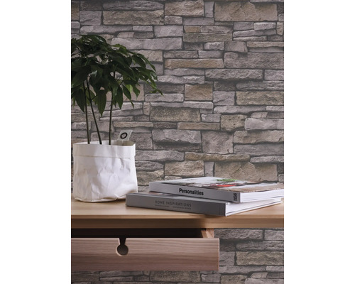 Close-up van een behang met steeneffect in een kamer met een plant en boeken op een tafel.