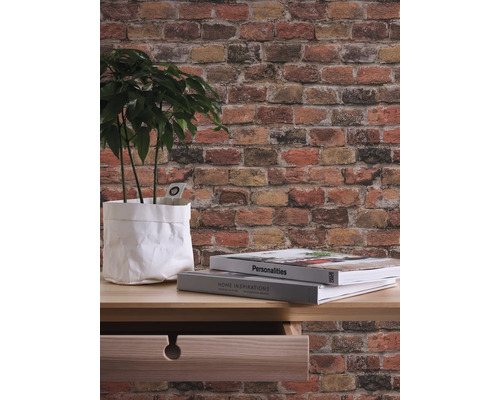 Behang met baksteenmotief, plant in papieren zak, boeken op tafel