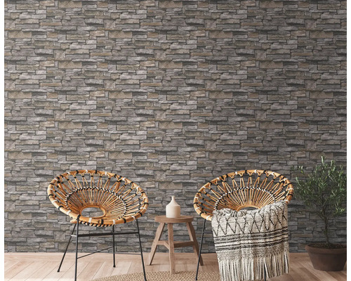 Twee rotan stoelen voor een muur met steenlook behang in een lichte kamer.