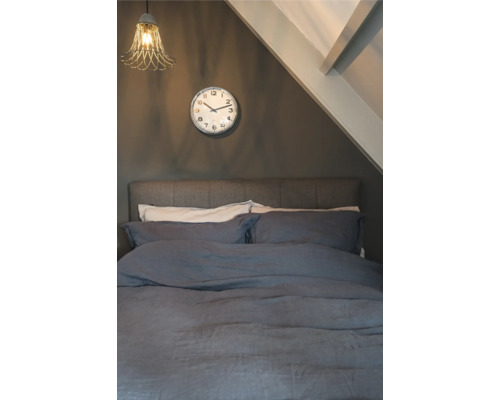 Slaapkamer met bed, klok en lamp onder een schuin dak