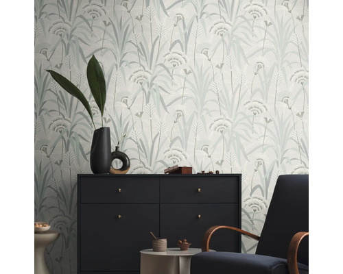 Een kamer met een patroonbehang met een bloemmotief, een commode en een fauteuil.