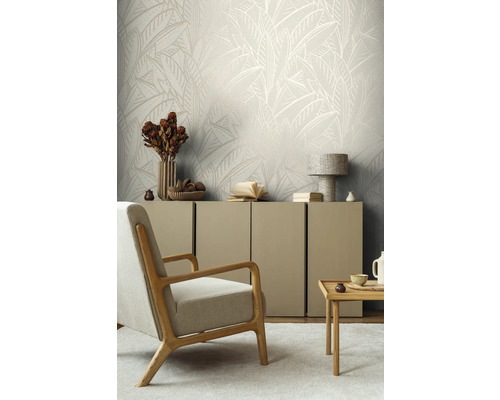 Woonkamer met beige behang met bladeren, fauteuil en dressoir.
