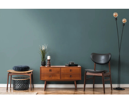 Woonkamer met houten ladekast, stoel, kruk en staande lamp op parketvloer