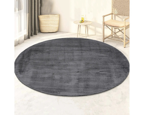 Grijs, rond vloerkleed in kamer met rotan stoel en tafel