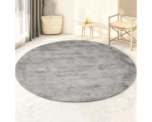 Rond grijs tapijt in de woonkamer met mand, tafel en stoel.