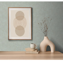 Decoratieve afbeelding met geometrische vormen in een houten lijst, samen met een vaas met takken, een kop en boeken op een tafel.