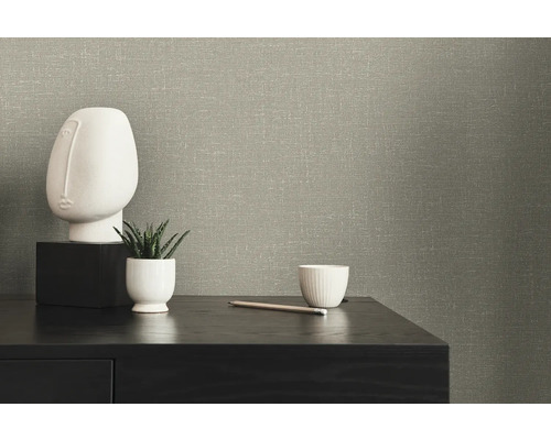 Close-up van een muur met gestructureerd behang, een decoratief gezicht, een vetplant en een kopje op een tafel.