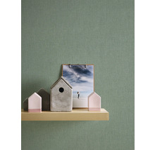 Decoratieve scène met houten plank, decoratieve huisjes en klembord tegen een groene wand