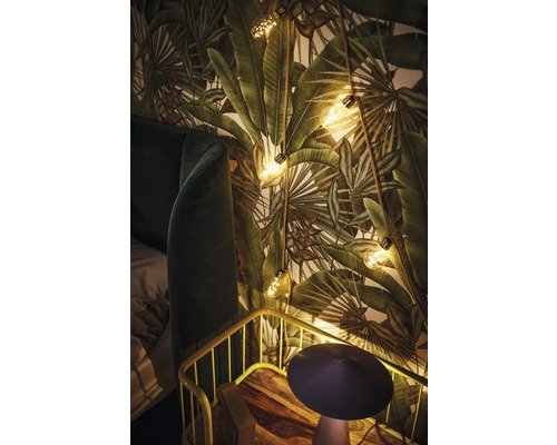 Decoratieve slaapkamer met behang met plantenmotief, lichtsnoer en nachtkastje.