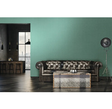 Woonkamer met leren bank, salontafel en staande lamp voor een muur met groen behang