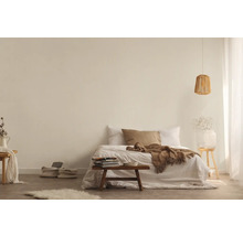 Lichte slaapkamer met bed, deken, kussens, bijzettafel, lamp en decoratieve elementen voor een vriendelijke sfeer.