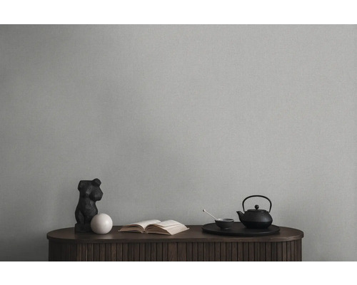 Decoratief stilleven met theepot, boek en sculptuur op een houten kast voor een effen muur.