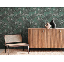 Woonkamer met groen behang met pauwenmotief, houten dressoir en stoel met webbing