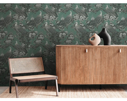 Woonkamer met groen behang met pauwenmotief, houten dressoir en stoel met webbing