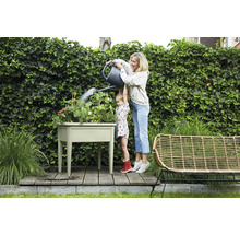 Een vrouw geeft met haar dochter een kruidentuin water in een verhoogde tuinbak in de tuin.