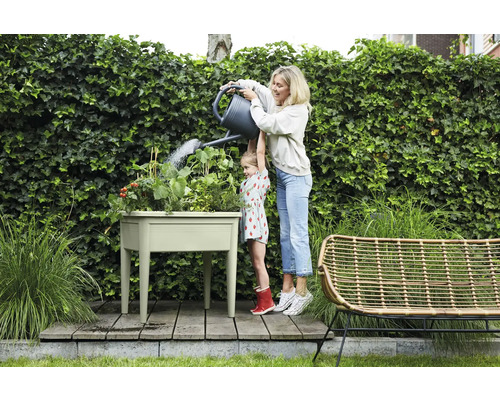 Een vrouw geeft met haar dochter een kruidentuin water in een verhoogde tuinbak in de tuin.