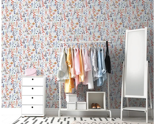 Inrichtingsvoorbeeld van een kamer met een witte commode, een kledingrek met kleding, een spiegel en een bloemetjesbehang.
