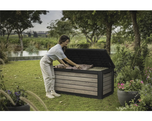 Een vrouw ruimt een tuinkist in de tuin in. De tuinkist is gemaakt van hout en kunststof.