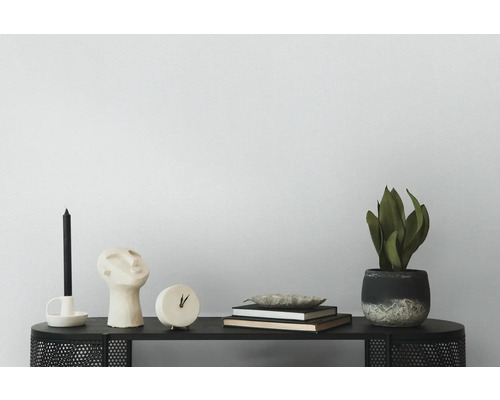 Decoratieve scène met kaars, sculptuur, klok, boeken, schaal en potplant op een zwarte tafel.