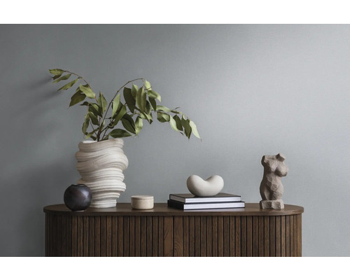 Decoratieve schikking op een houten kast met vaas, groene planten, boeken en sculpturen.