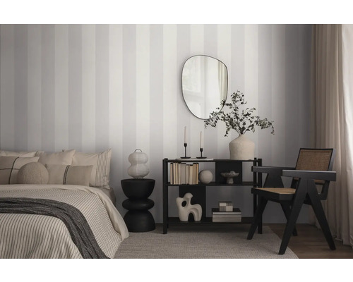 Slaapkamer met bed, rek, spiegel en gestreept behang.