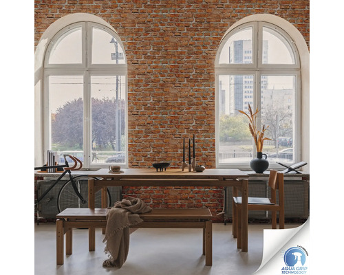 Eetkamer met houten tafel, bank en stoel voor een bakstenen muur met twee grote ramen